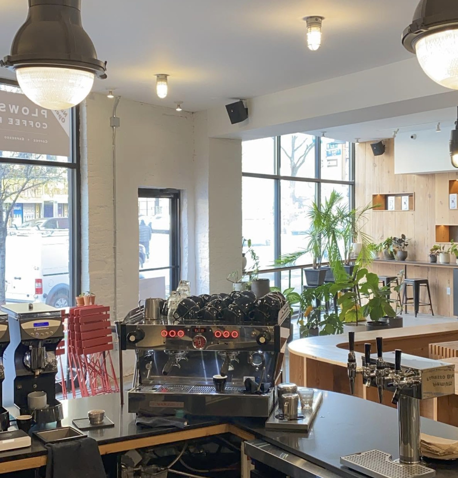 The espresso bar and taps at Plowshares Coffee Roasters with plant lined seating behind